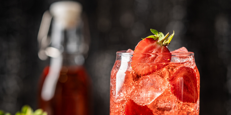 A tall, refreshing red drink filled with ice and fresh strawberry slices, highlighting the final strawberry syrup result.