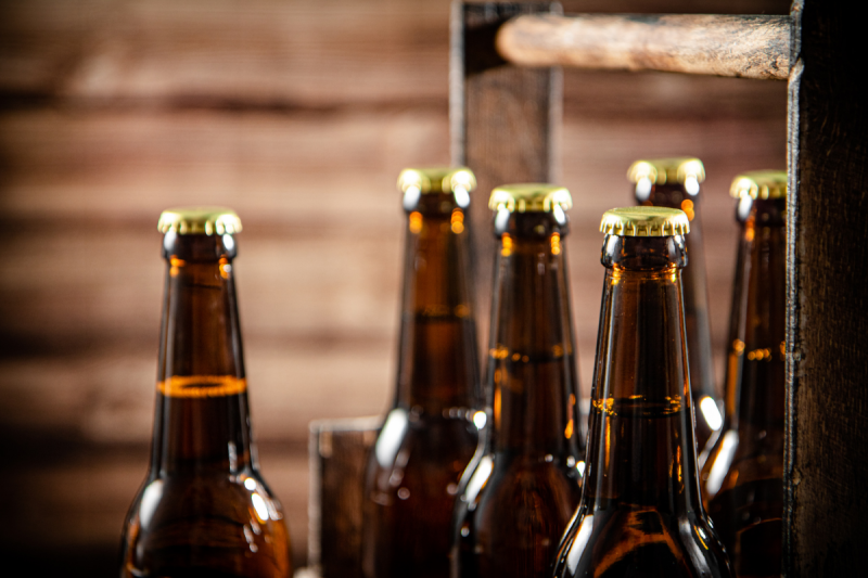 Close-up of brown glass beer bottles with gold caps arranged in a vintage wooden carrier box.